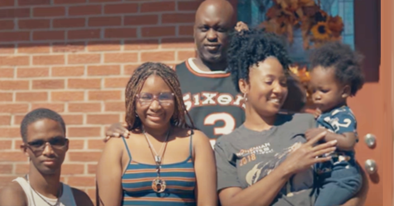 A family of 5 stand in front of their brick home.